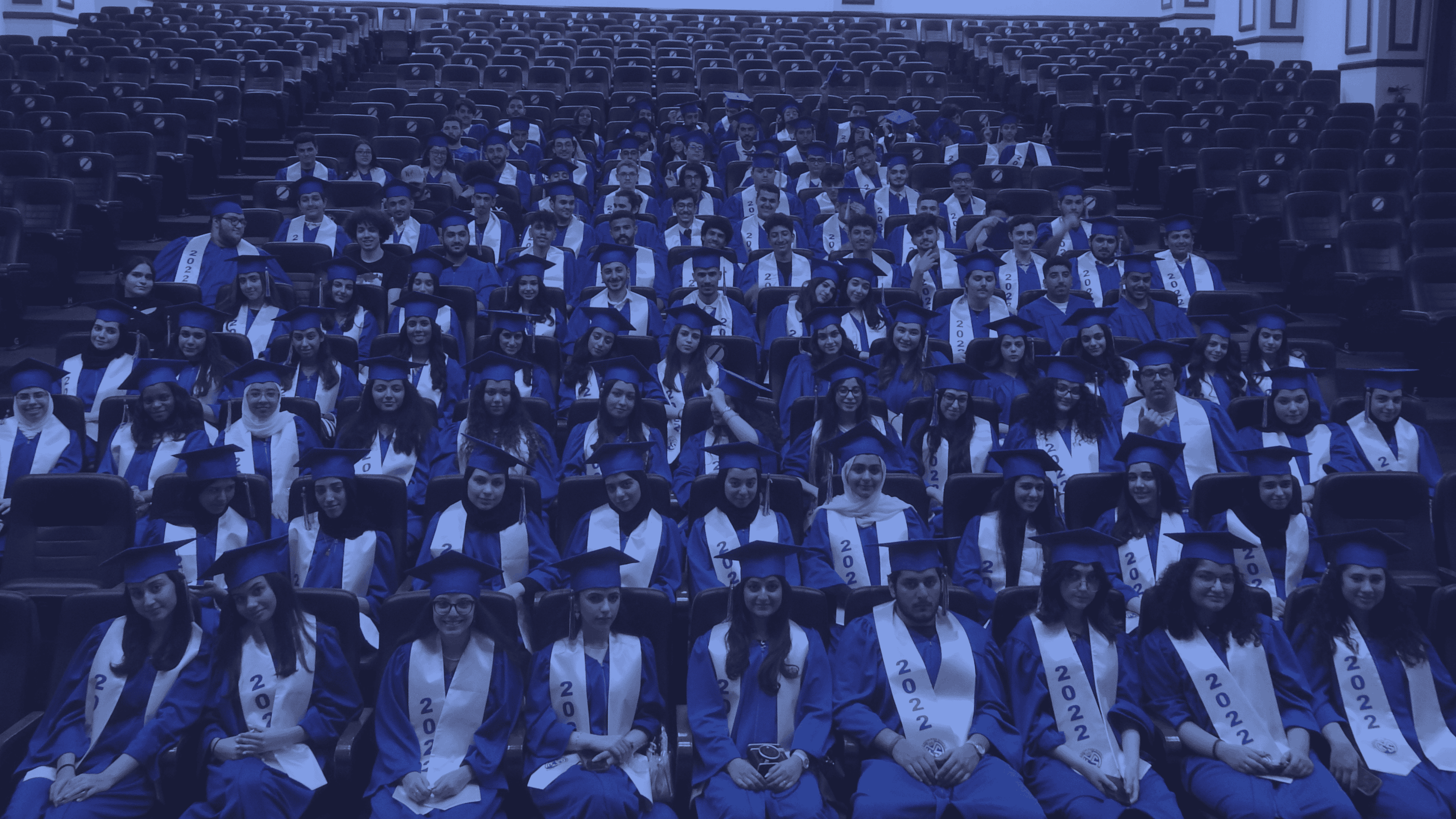 Graduates in blue caps and gowns at a university commencement ceremony, celebrating academic achievement and graduation day, with students seated in an auditorium.
