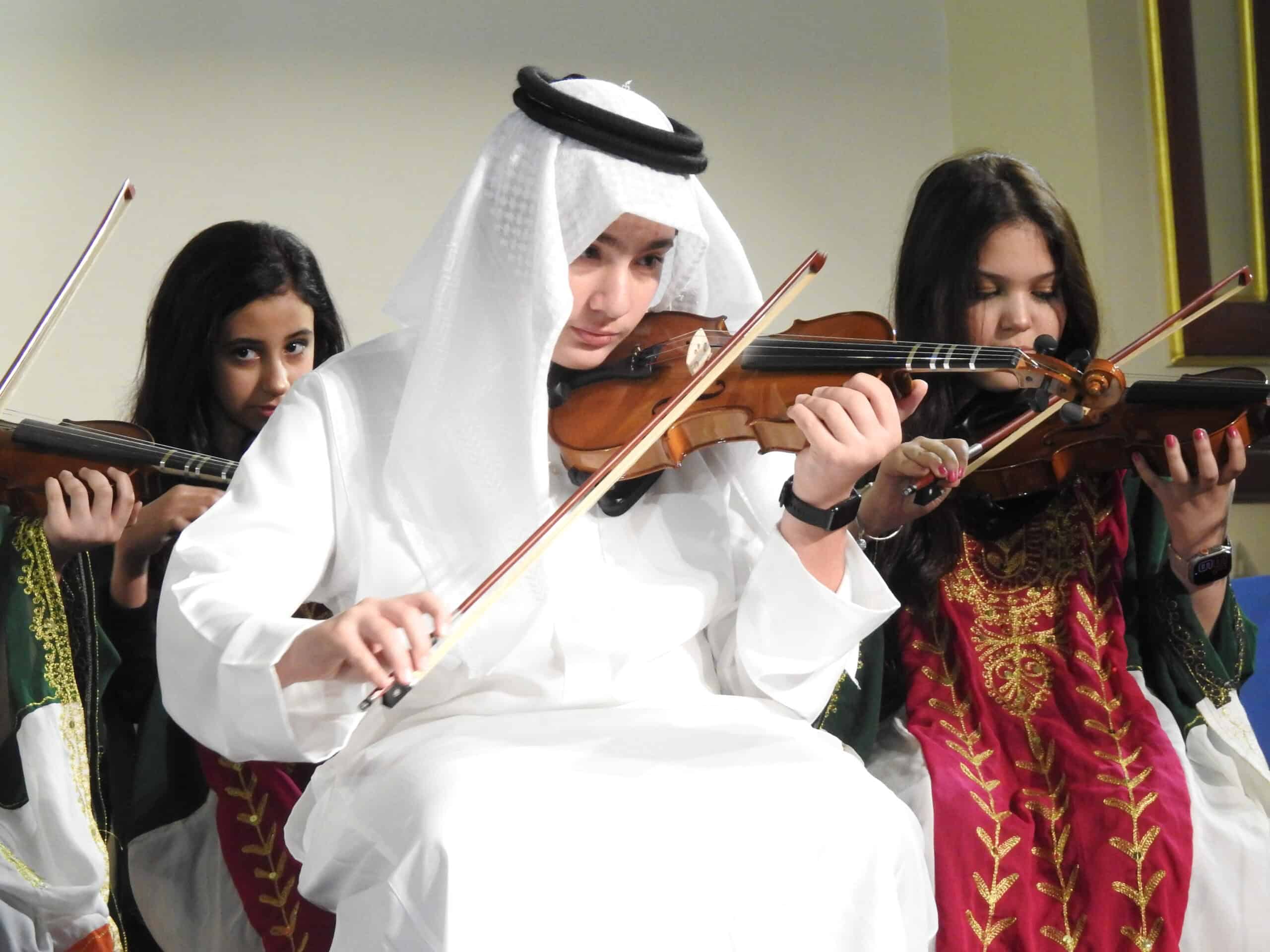 Children playing violins in cultural attire at MKS educational institution.
