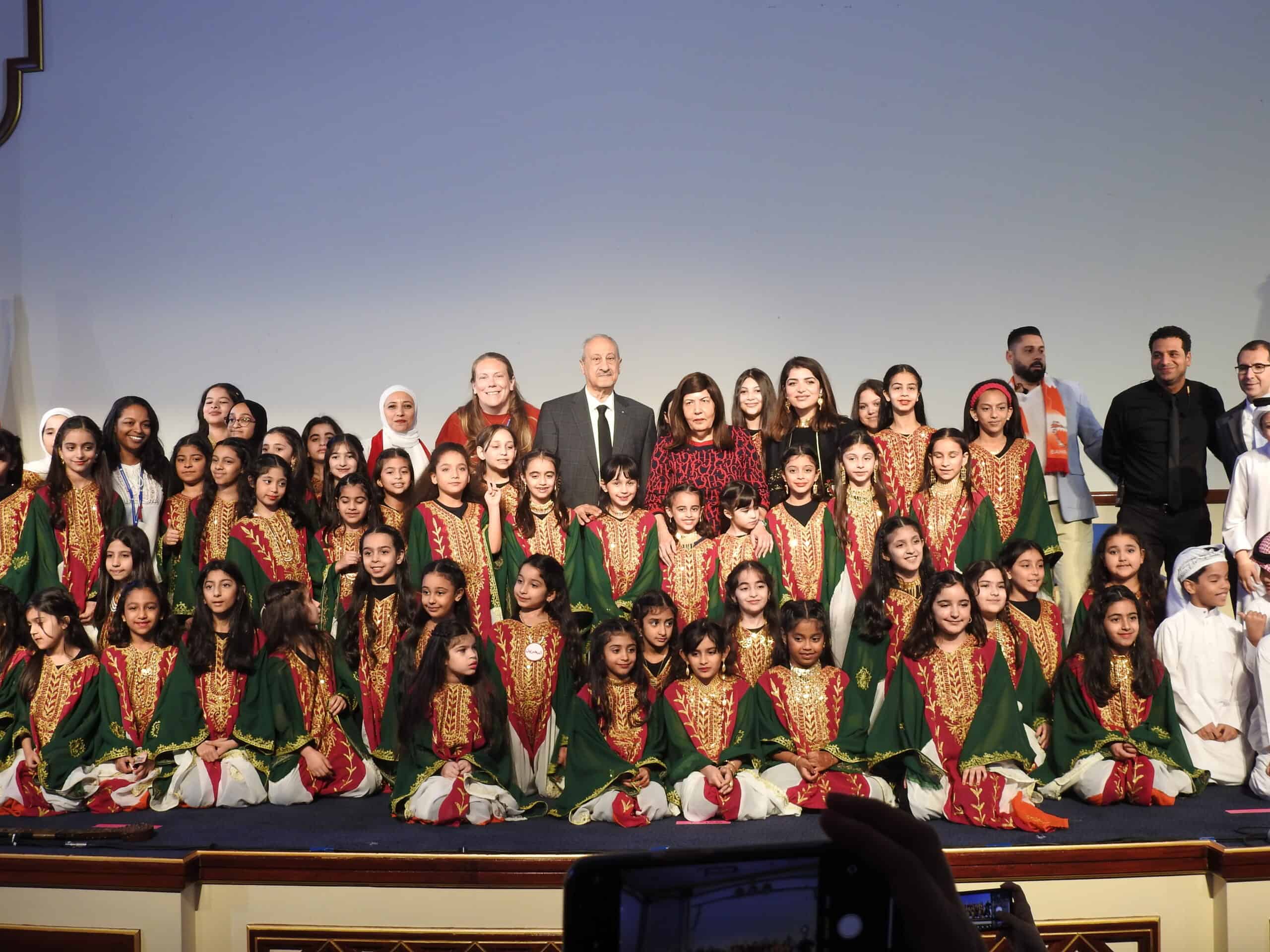 Children performing at an event on stage, dressed in traditional costumes with school officials and teachers celebrating cultural heritage and the success of educational programs at MKS, Bahrain.