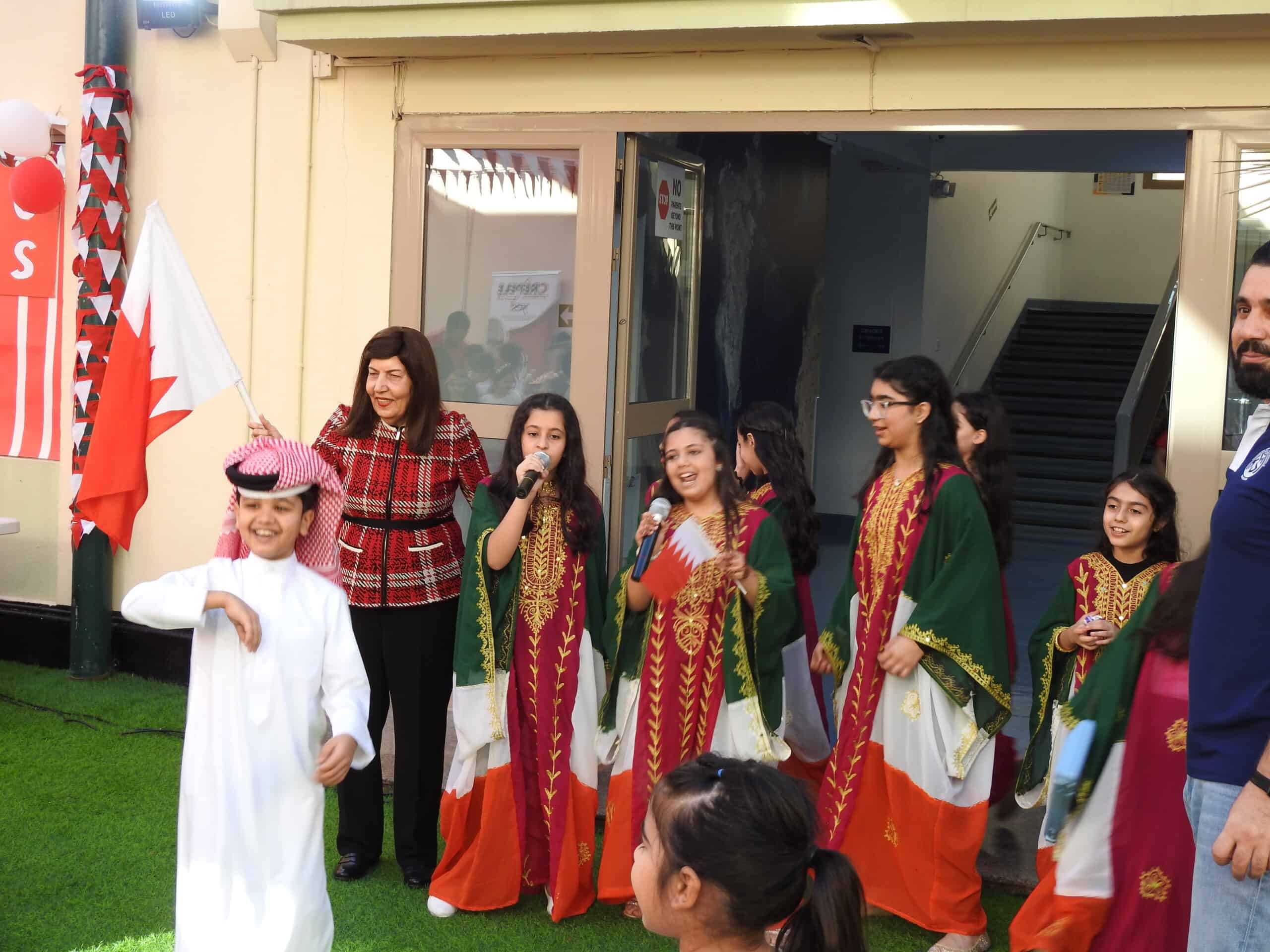 Celebration of Bahrain National Day at MKS School with children in traditional costumes, waving Bahraini flags, and participating in cultural performances, emphasizing national pride and heritage.